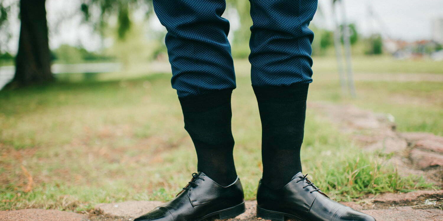 Unrecognizable man in wedding suit standing outdoor with socks put on trousers. Groom in black leather shoes standing on nature at stone. Freaky, foolish, absurd, odd clothes style. Funny marriage day Ingenia Asignatura de Industriales UPM